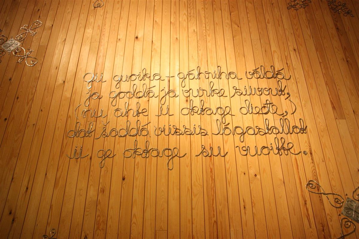 Foto av kunst på en vegg i Sametinget, hvor et ordtak er hamret i tinntråd direkte på vegg. - Klikk for stort bilde
